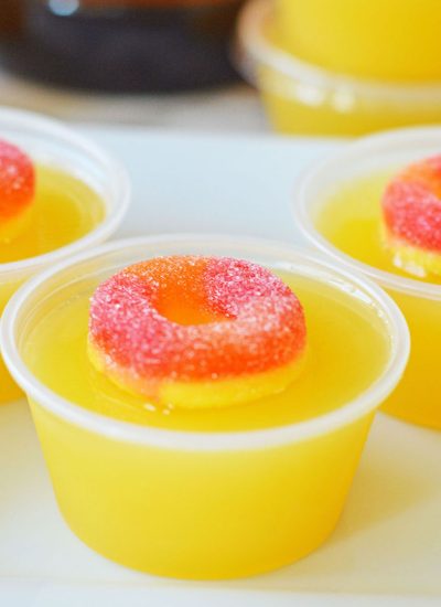 closeup of a fuzzy navel jello shot topped with a peach ring candy.