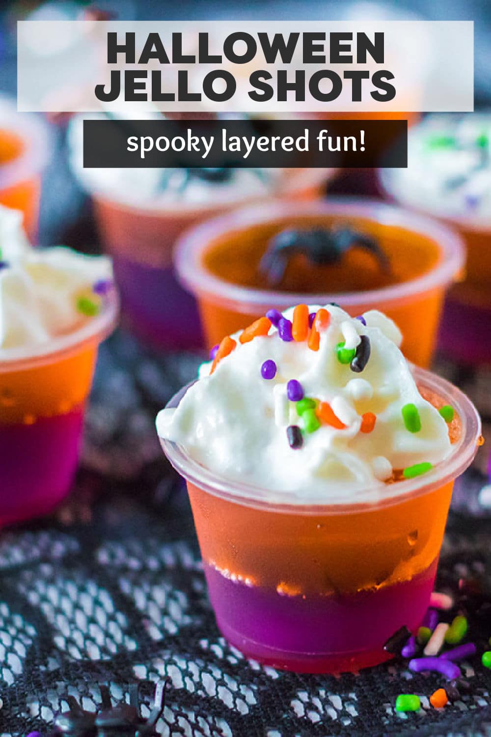 Perfectly spooky layered Halloween Jello Shots are made with vodka and will be a huge hit at your next Halloween party. Orange and purple jello are layered together then topped with whipped cream, Halloween sprinkles, and chocolate spider webs. Simple to make and fun to enjoy! | www.persnicketyplates.com