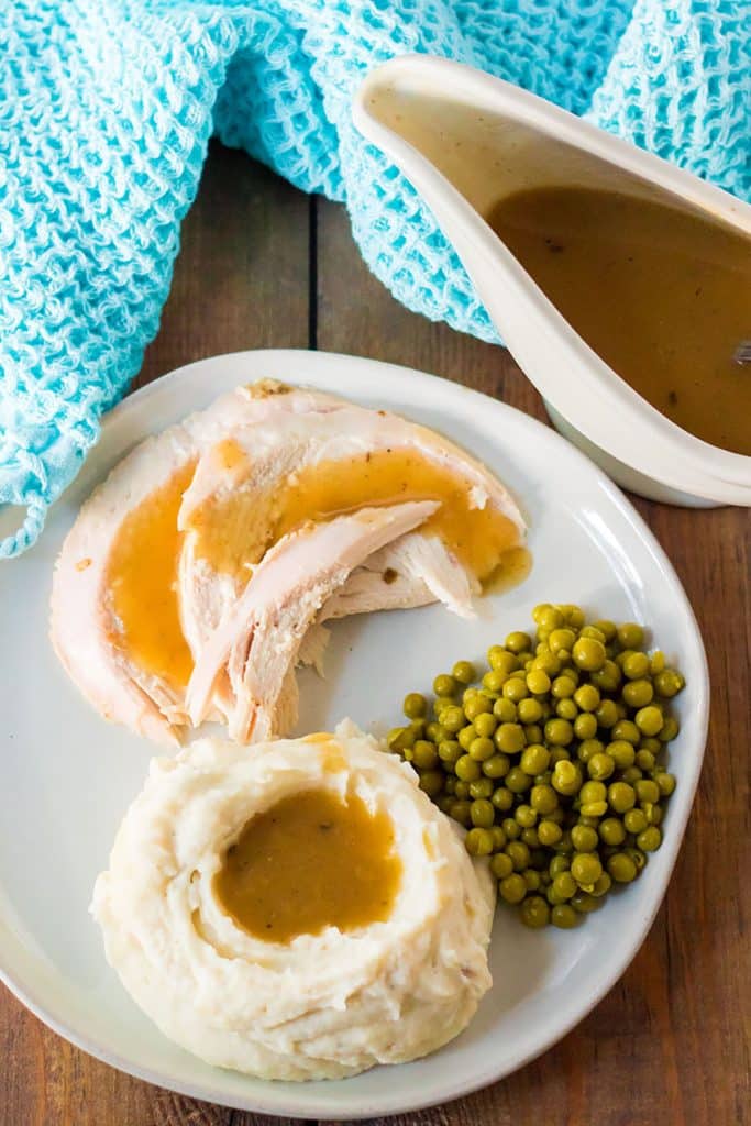overhead shot of dinner plate with mashed potatoes, turkey, gravy, and peas next to a gravy boat.