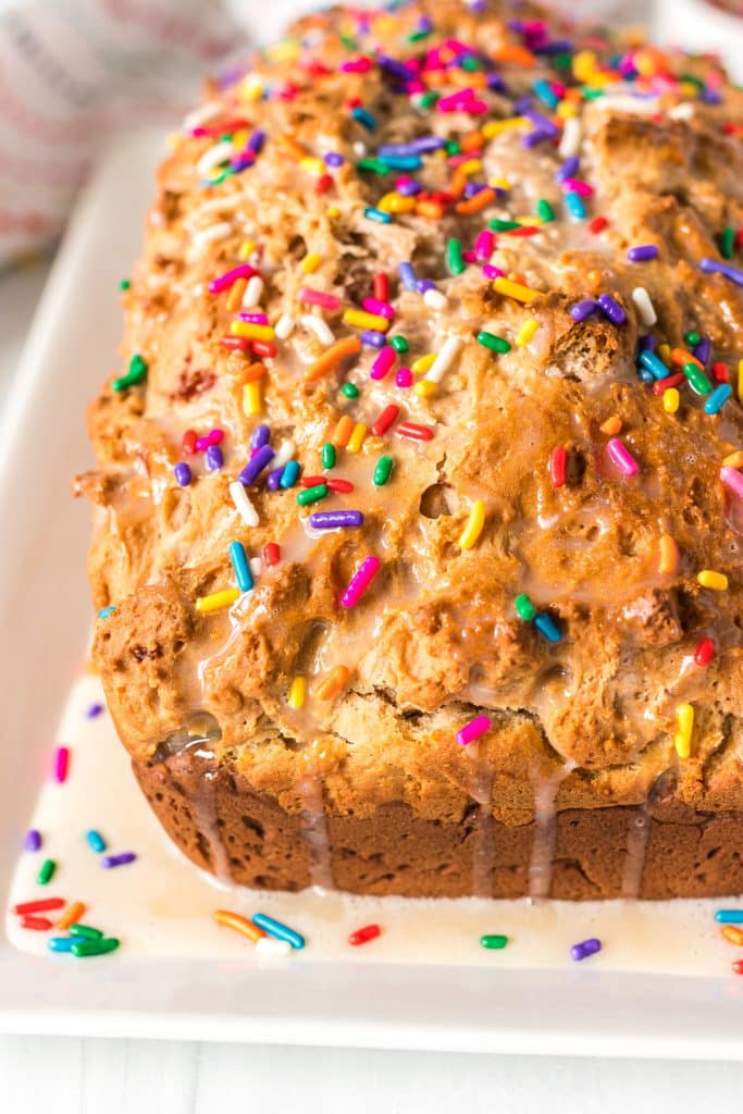corner of an ice cream bread loaf topped with glaze and rainbow sprinkles.