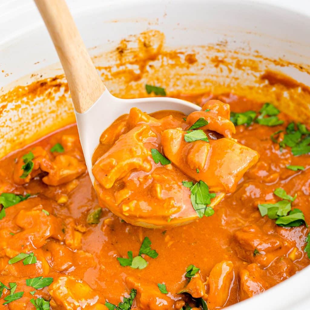 a ladle scooping butter chicken out of a crockpot.