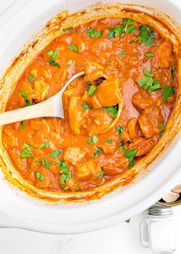 a ladle scooping butter chicken from a slow cooker.