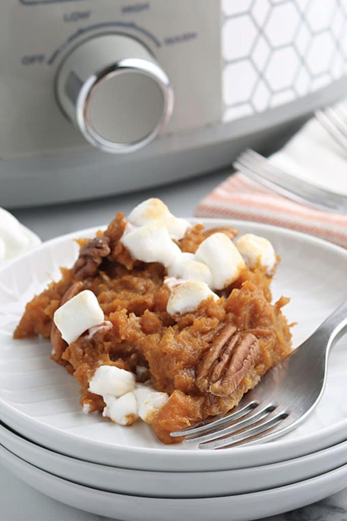 scoop of sweet potato casserole topped with marshmallows and pecans on a white plate.