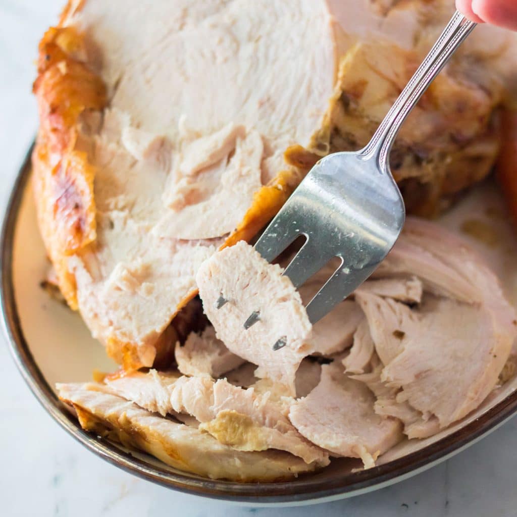 fork lifting a slice of turkey breast from a plate.