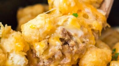 wooden spoon dipping into cheesy tater tot casserole in a crockpot.