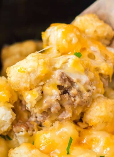 wooden spoon dipping into cheesy tater tot casserole in a crockpot.