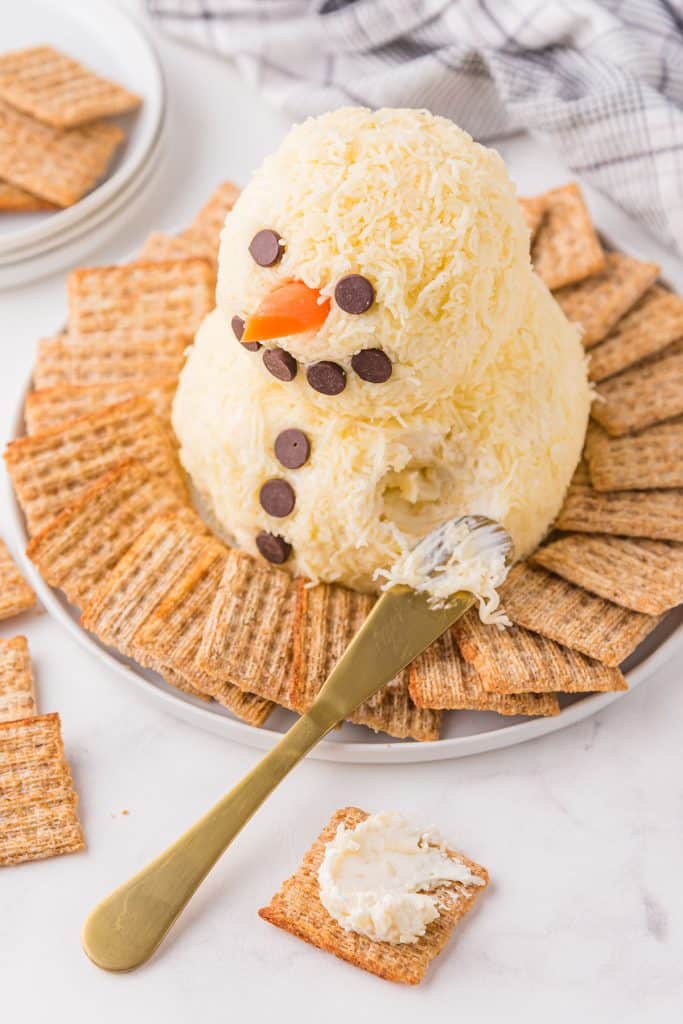 cheese knife putting cheese on a triscuit from a snowman cheese ball.