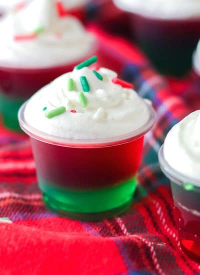 red & green christmas jello shot topped with whipped cream & sprinkles.