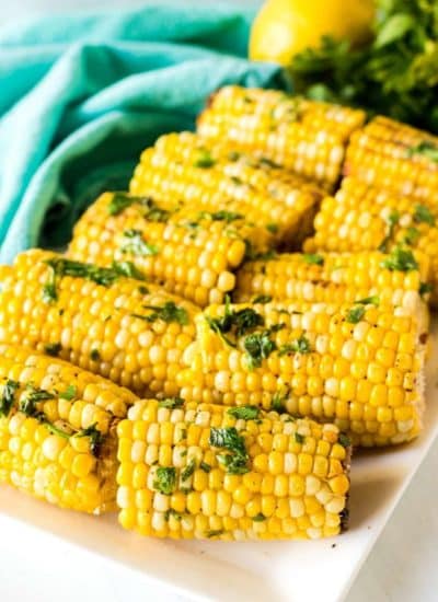 white platter of corn on the cob topped with parsley.