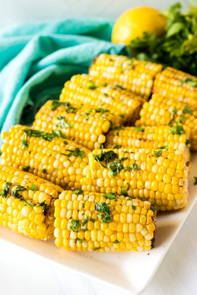 white platter of corn on the cob topped with parsley.