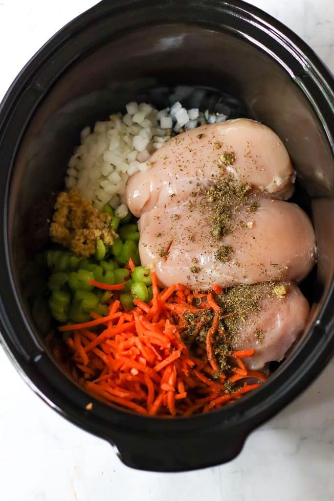 overhead shot of raw chicken onions, carrots in a slow cooker.