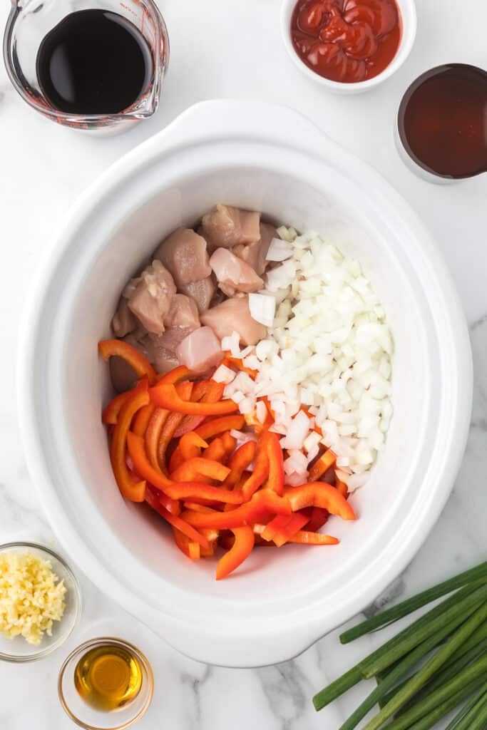overhead shot of onions, peppers, and raw chicken in a slow cooker.