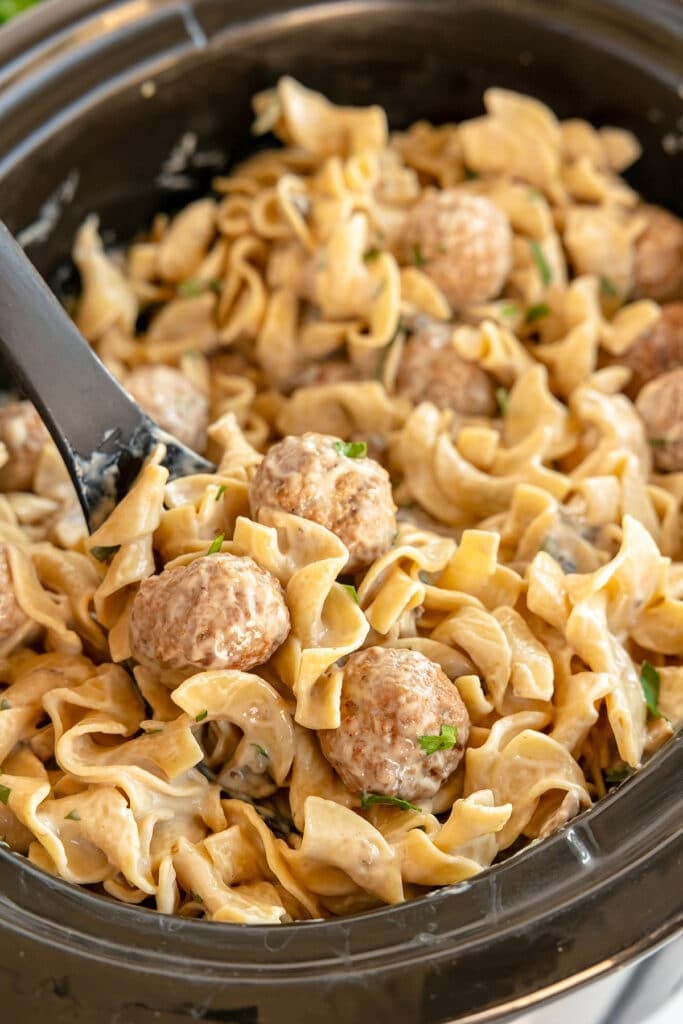 spoon lifting meatball stroganoff from a slow cooker.
