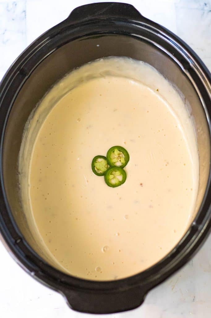 overhead shot of queso in a slow cooker topped with jalapenos.