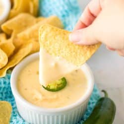 hand dipping a tortilla chip into queso.