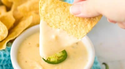 hand dipping a tortilla chip into queso.