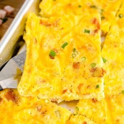 sheet pan eggs with ham being lifted with a spatula.