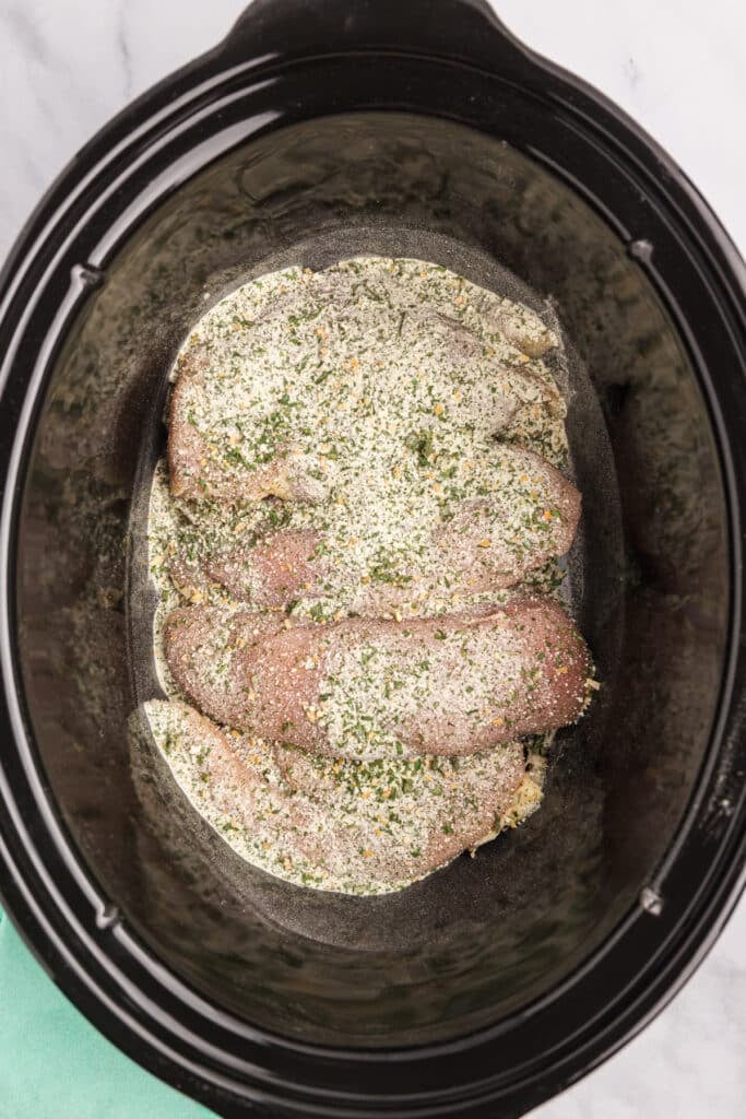 overhead shot of chicken breasts sprinkled with ranch seasoning in a crockpot.