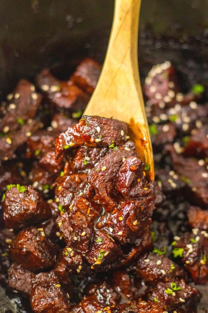 wooden spoon scooping steak bites from a slow cooker.