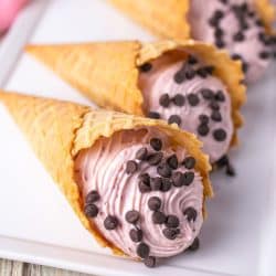 strawberry cannoli cones topped with mini chocolate chips laying on a white platter.
