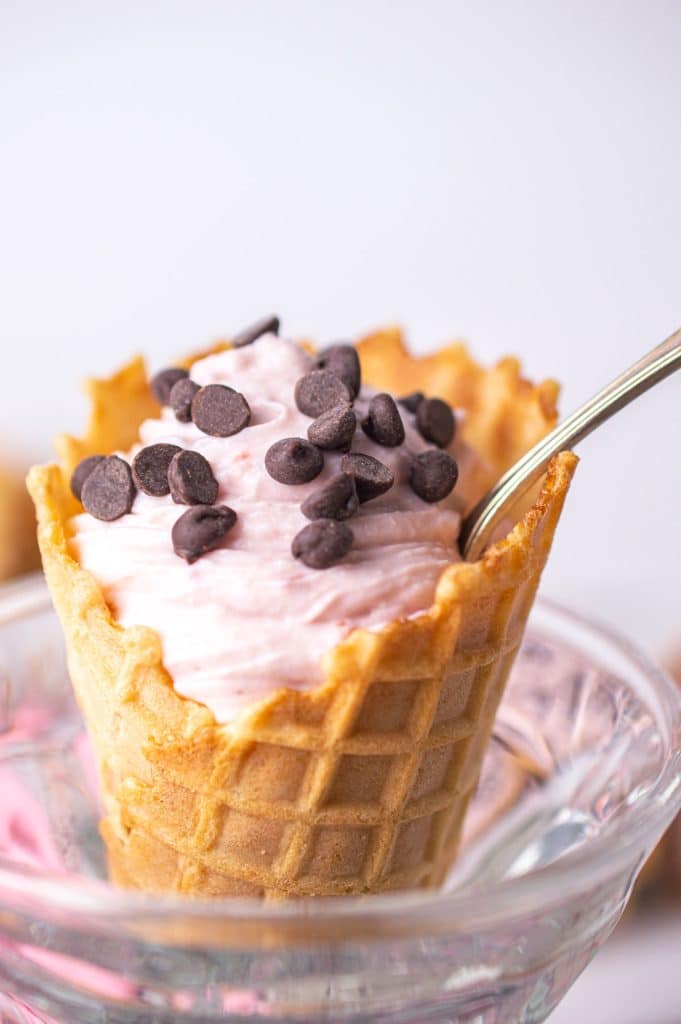 spoon dipping into a waffle cone filled with cannoli filling.