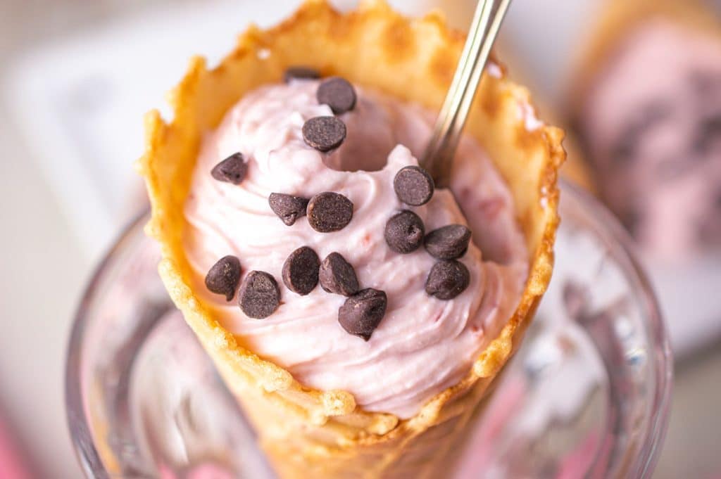 spoon dipping into a strawberry cheesecake filled waffle cone.
