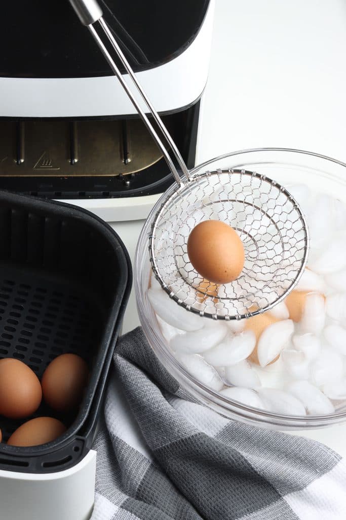 a slotted spoon moving eggs from an air fryer to an ice bath.