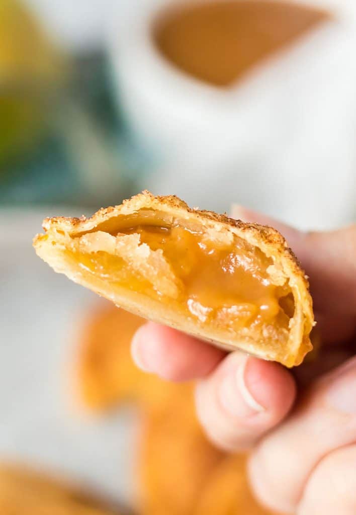 hand holding a caramel apple empanada with a bite missing.