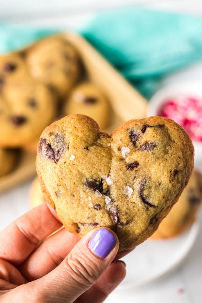 hand holding a heart shaped chocolate chip cookie.