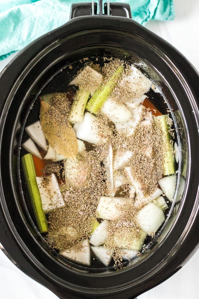 overhead shot of slow cooker with vegetables and seasonings for stock.