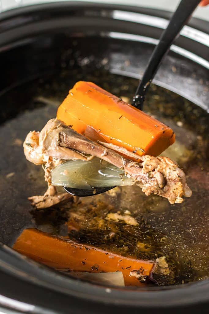 spoon scooping chicken bones & carrots from a slow cooker.