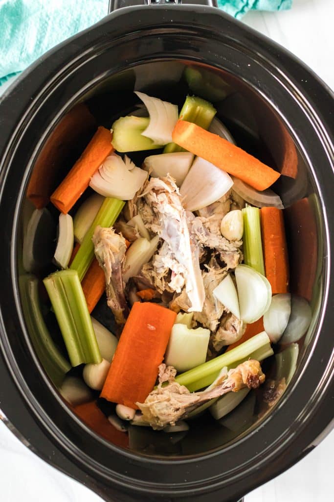 overhead shot of chicken carcass & vegetables in a slow cooker.