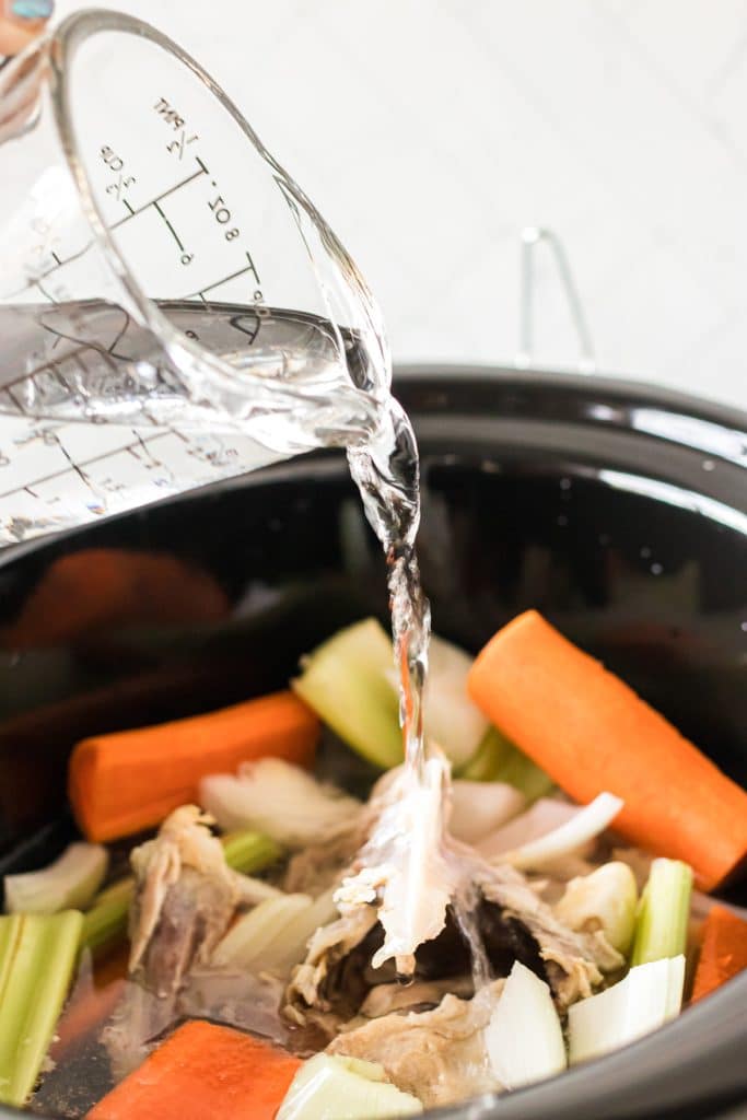 water being poured into a crockpot of vegetables.