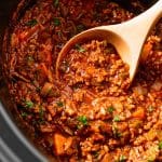 wooden spoon scooping spaghetti sauce from a slow cooker.