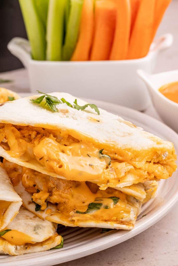 side view of a buffalo chicken quesadilla in front of a cup of carrots & celery.