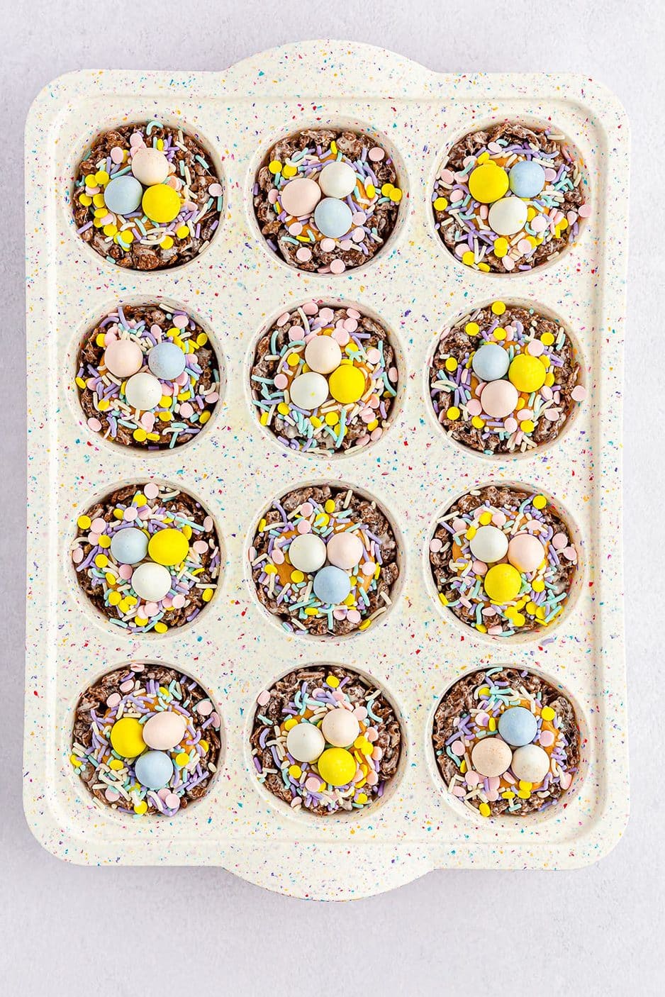 overhead shot of chocolate bird nest cookies in a cupcake tray topped with cadbury eggs and sprinkles.
