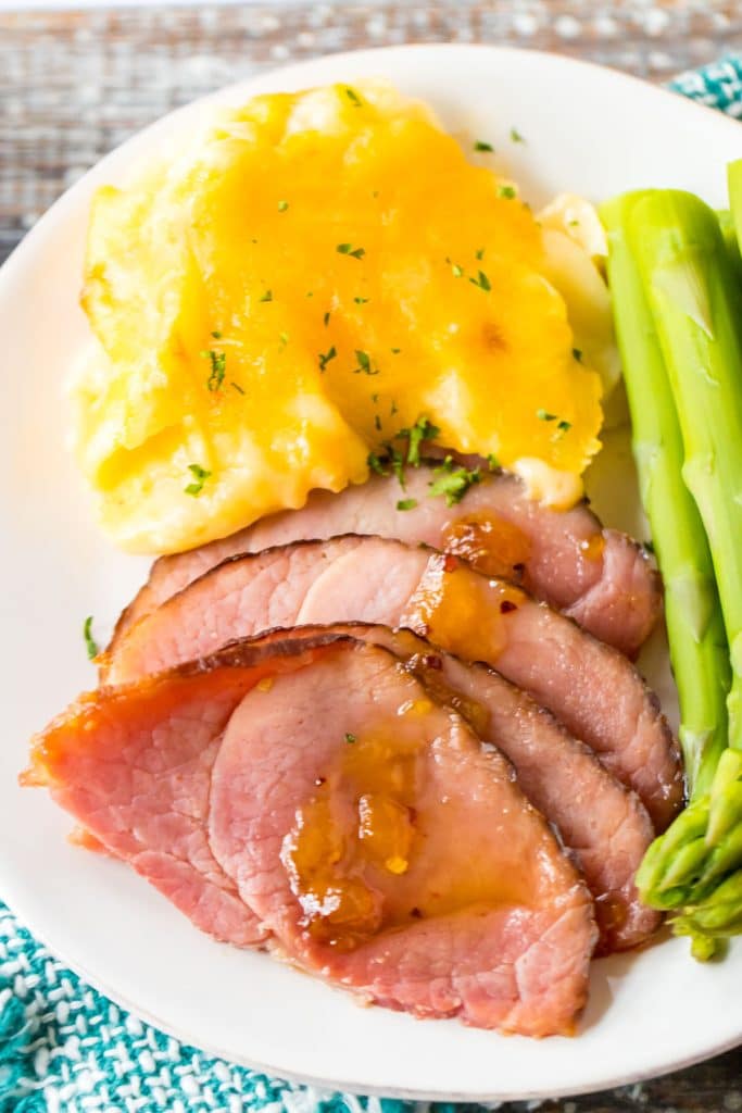 overhead shot of a white plate filled with sliced ham, cheesy potatoes, and asparagus.