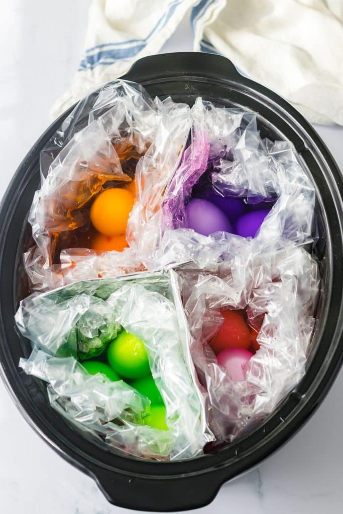 overhead shot of a slow cooker with dyed green, orange, pink, and purple easter eggs.