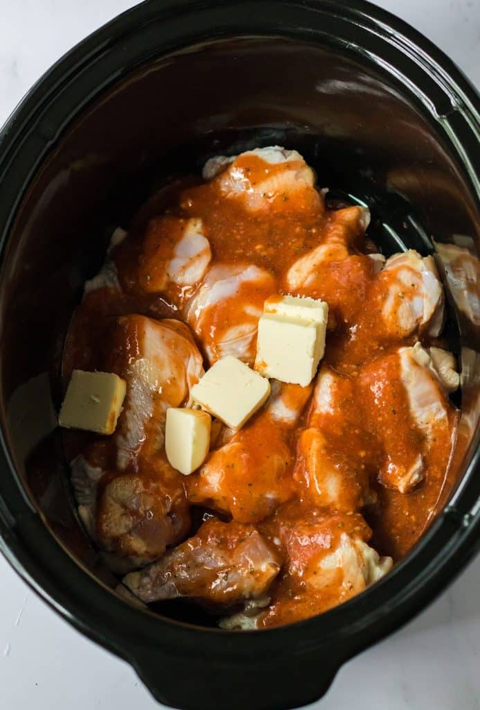 overhead shot of chicken wings in a slow cooker topped with cubes of butter.