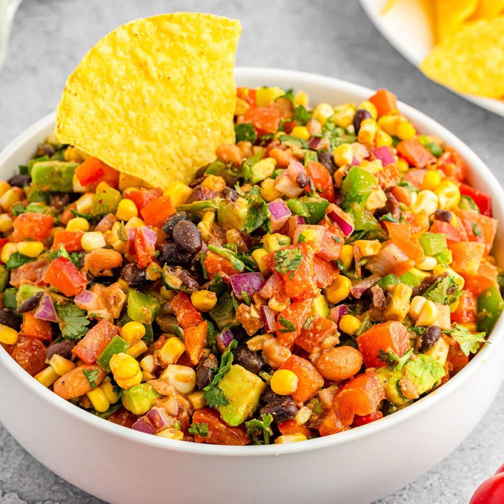 white bowl of cowboy caviar dip with a tortilla chip dipped in.