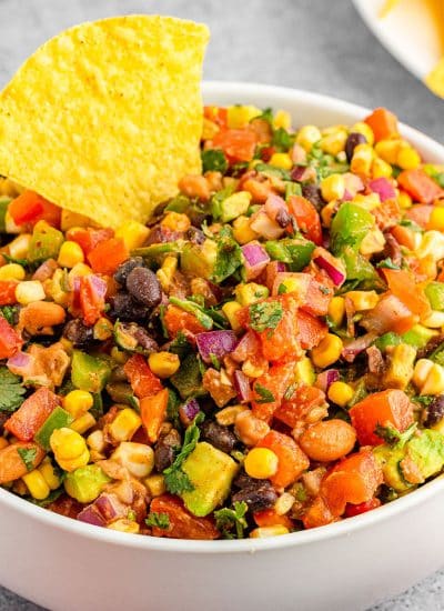 white bowl of cowboy caviar dip with a tortilla chip dipped in.