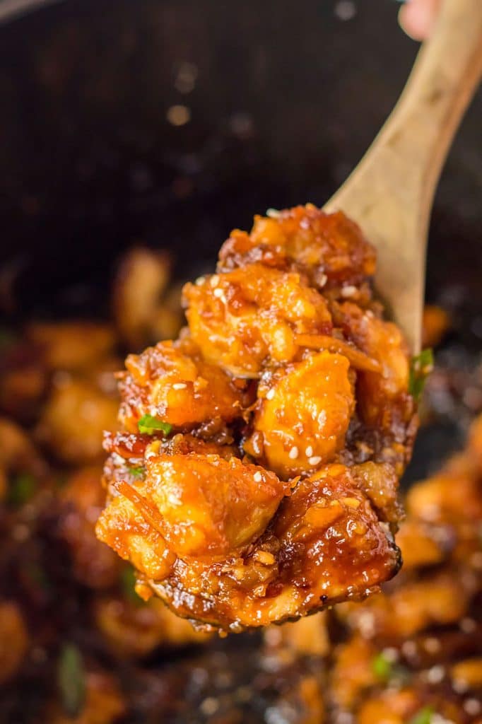 wooden spoon scooping orange chicken from a slow cooker.