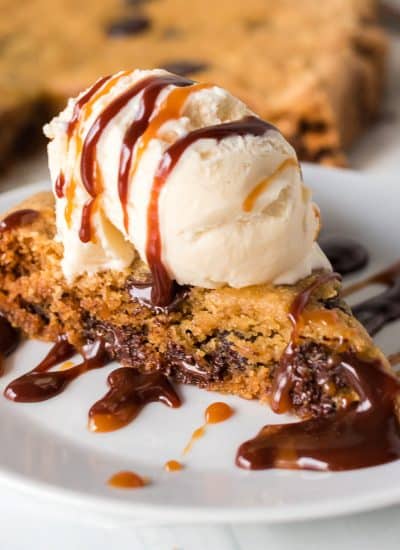 slice of chocolate chip cookie cake topped with ice cream and hot fudge.