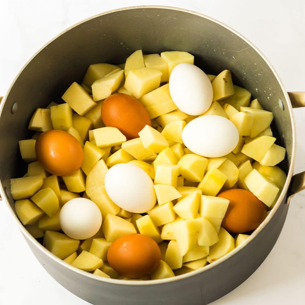 overhead shot of diced potatoes & whole eggs in a pot.