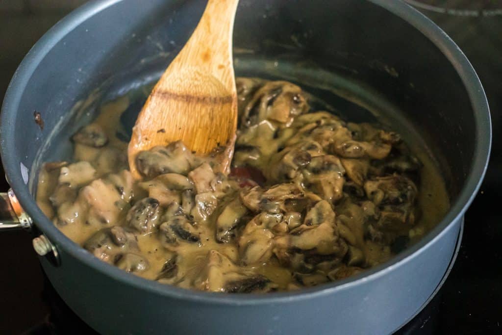 wooden spoon stirring mushrooms in a skillet.