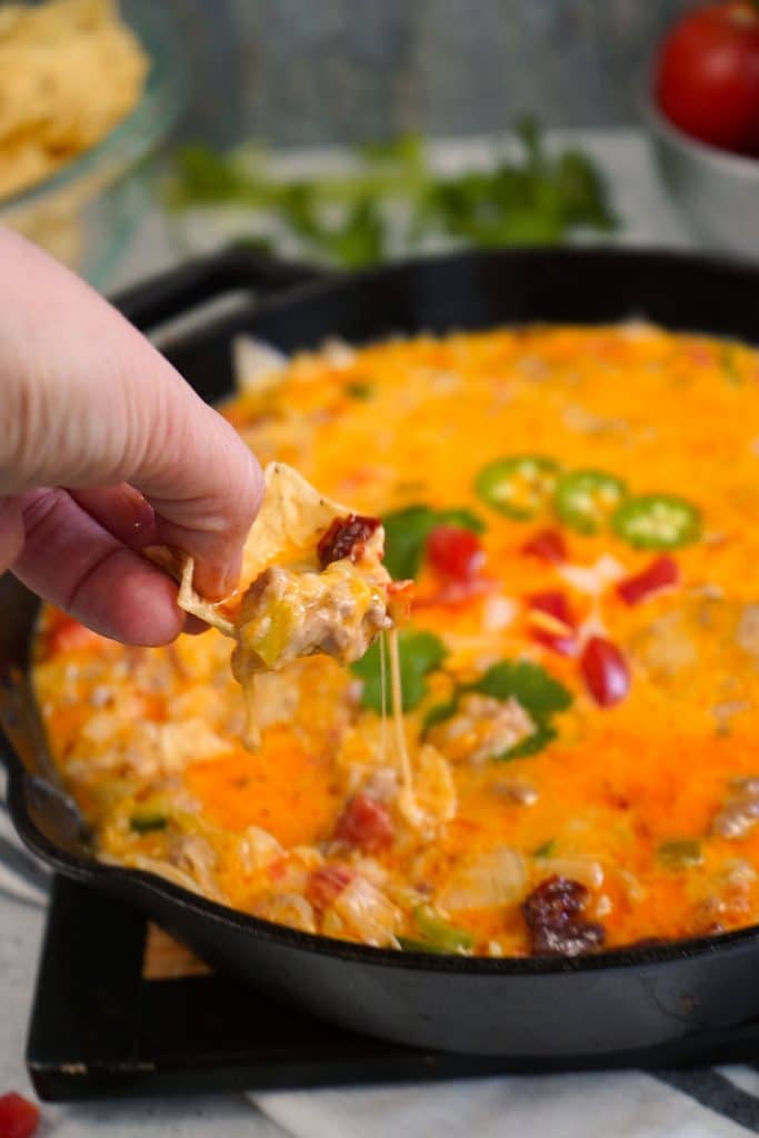 hand lifting a tortilla chip from a skillet of queso.