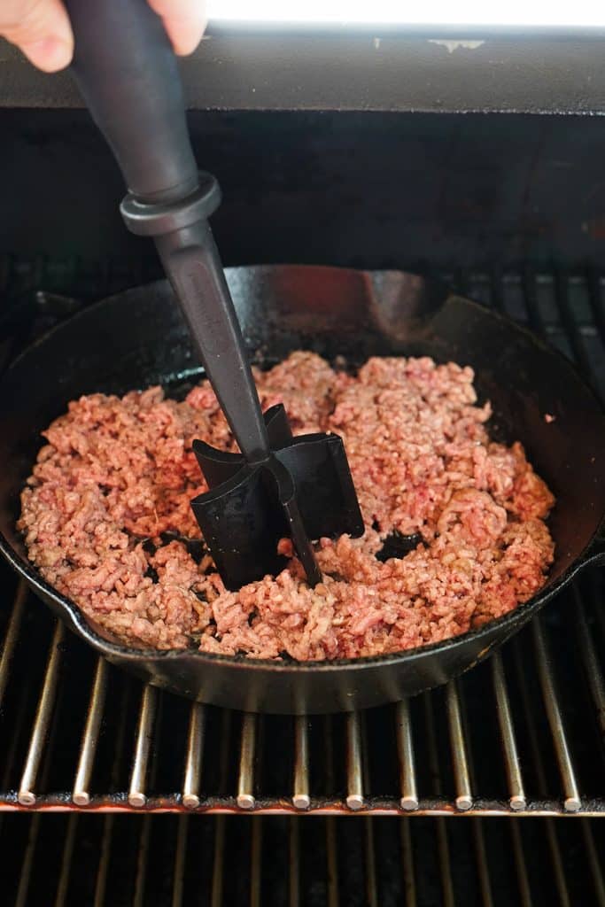 meat chopper breaking up ground beef in a cast iron skillet.