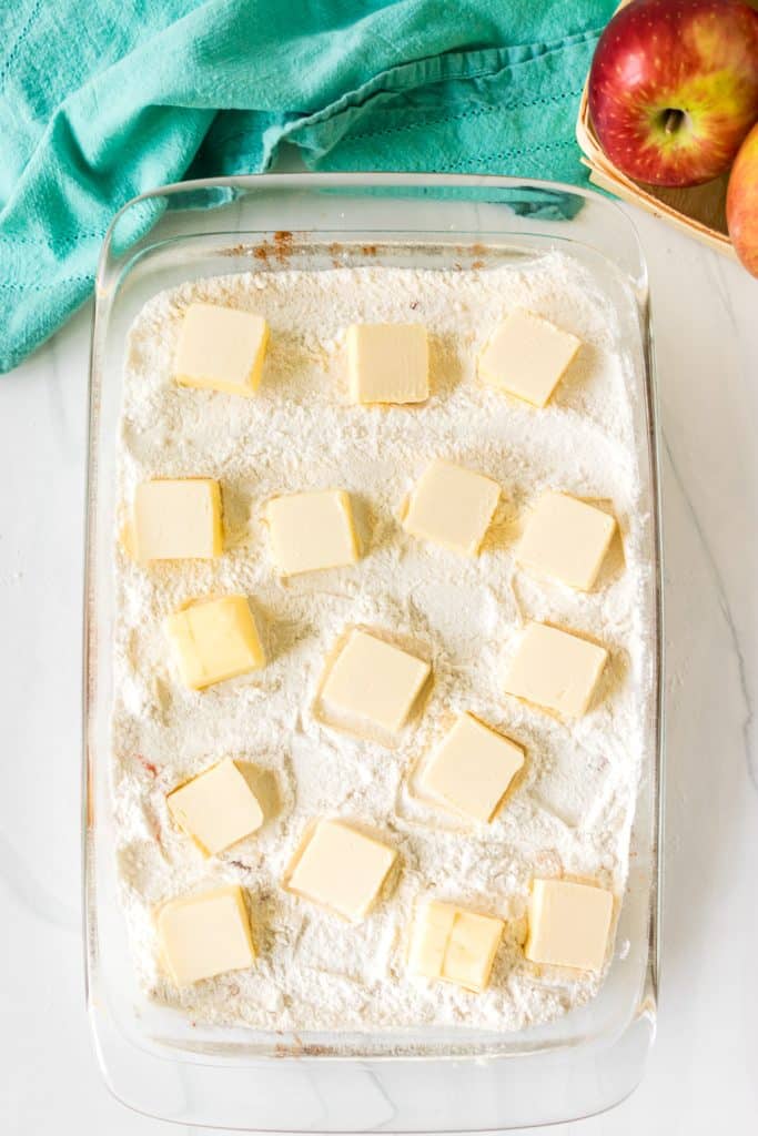 overhead shot of cake mix topped with squares of butter in a baking dish.