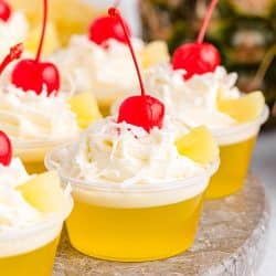 side view of pina colada jello shots garnished with whipped cream & cherries.