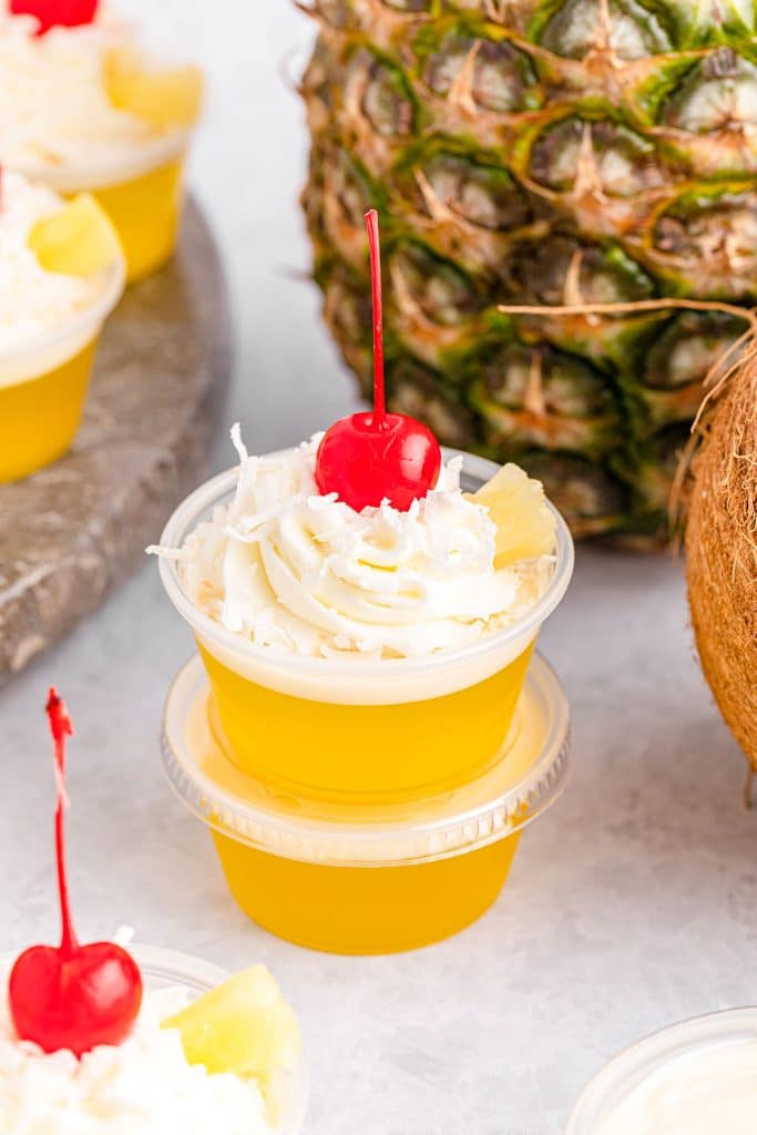stack of 2 pina colada jello shots in front of a pineapple.